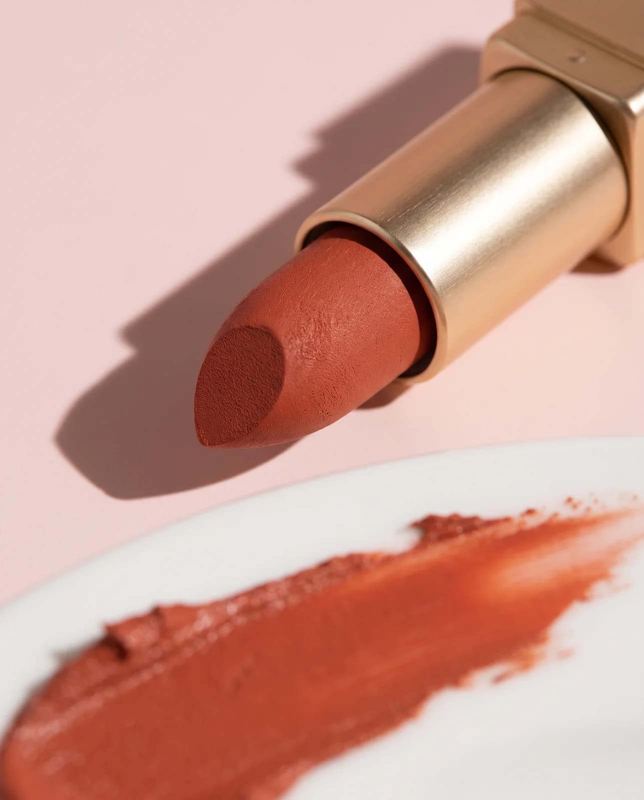 Terracotta lipstick with a swatch on pink paper